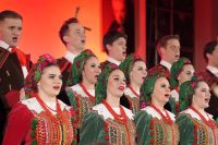 Śpiewające kobiety i mężczyźni ubrani w różnokolorowe stroje ludowe.