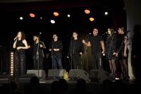 Trzy kobiety i czterech mężczyzn stojących na scenie przy mikrofonach.