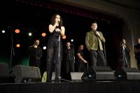 Trzy kobiety i czterech mężczyzn stojących na scenie przy mikrofonach.