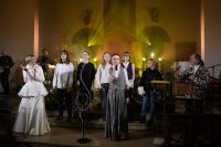 Dwie kobiety z mikrofonami stojące wraz z młodzieżą w kościele.