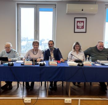 Sala konferencyjna, kilka osób siedzących przy stole patrzy w obiektyw