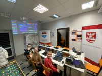 Trójka dzieci siedzących przy stole z laptopami. Przed nimi dwa rollupy.