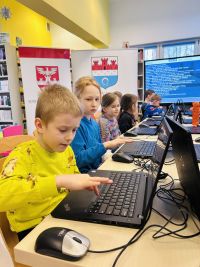 Dzieci pracujące na laptopach. Za nimi dwa rollupy.