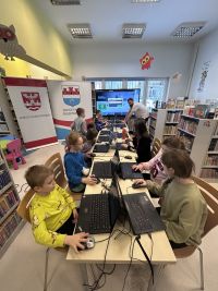 Dzieci pracujące na laptopach. Po lewej stronie dwa rollupy.