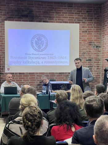 wykład w murach muzeum, zebrani wysłuchujący wykładu, prezentacja wyświetlana na ścianie