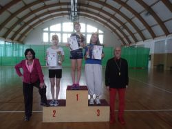 Dziewczynki stojące na podium w koronach, trzymające w rękach puchary i dyplomy, obok nich kobieta i mężczyzna.