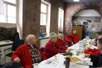 Kobieta i mężczyźni siedzący przy stole z ciastem, ciasteczkami i wodą.