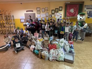 grupa dzieci pozująca do zdjęcia, na podłodze leżą paczki, po prawej stronie stoi biały niedźwiedź