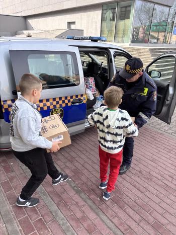 samochód straży miejskiej, chłopcy niosący paczki, strażnik umieszcza paczki w samochodzie