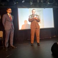 Mężczyzna w mundurze wojskowym trzymających w rękach mikrofon, po lewej stronie stoi mężczyzna w garniturze.