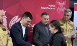 zgromadzona młodzież w strojach czarnych strojach pożarniczych, wręczanie nagród, w tle czerwona ścianka straży pożarnej