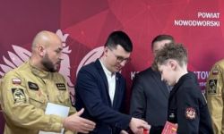 zgromadzona młodzież w strojach czarnych strojach pożarniczych, wręczanie nagród, w tle czerwona ścianka straży pożarnej