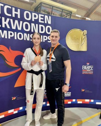 zawodniczka z trenerem pozuje do zdjęcia, w ręku trzyma medal