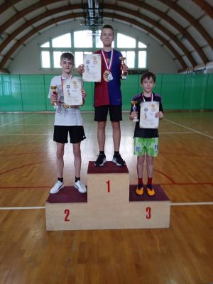 Chłopcy stojący na podium z medalami na szyjach, trzymający dyplomy i puchary w rękach.