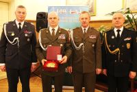 Czterech żołnierzy, jeden z nich trzyma w jednym ręku pudełko z dużym guzikiem, z orzełkiem, a w drugi medal.