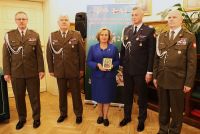 Kobieta trzymająca w rękach obrazek Matki Bożej Częstochowskiej, stojąca pomiędzy czteroma żołnierzami.