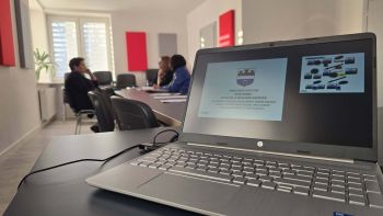 na pierwszym planie laptop z prezentacją, w tle sala z osobami