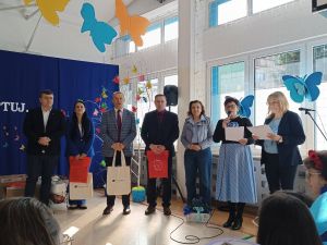 Trzech mężczyzn, dwóch z torbami, cztery kobiety, jedna z nich z torbami, druga z mikrofonem, trzecia z kartką.