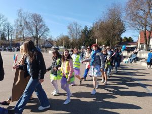 Dzieci i dorośli idący dwójkami, trzymając się za ręce.