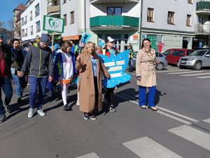 Dzieci i dorośli idący ulicą z motylami i transparetm z logotypem.