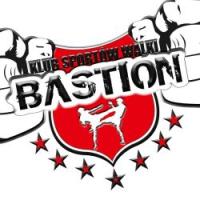 czerwona tarcza, postacie walczące, napis Bastion