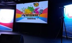 logo festiwalu wyświetlane na dużym ekranie, obok stoją rollupy organizatorów