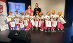 dzieci na scenie ubrane w jednakowe stroje, w rękach trzymają torby z upominkami