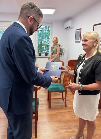 burmistrz wręcza teczkę z herbem miasta uśmiechniętej kobiecie