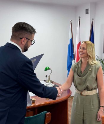 burmistrz wręcza teczkę z herbem miasta uśmiechniętej kobiecie