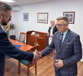 burmistrz wręcza teczkę z herbem miasta uśmiechniętemu mężczyźnie w okularach