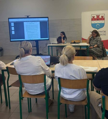 kilka osób siedzących tyłem, w tle rollup z logo miasta, ekran z prezentacją