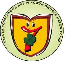 Żółta tarcza szkolna z oczami, uśmiechem utworzonym z czerwonej cyfry siedem, na któej znajduje się zielona, czterolistna koniczyna.
