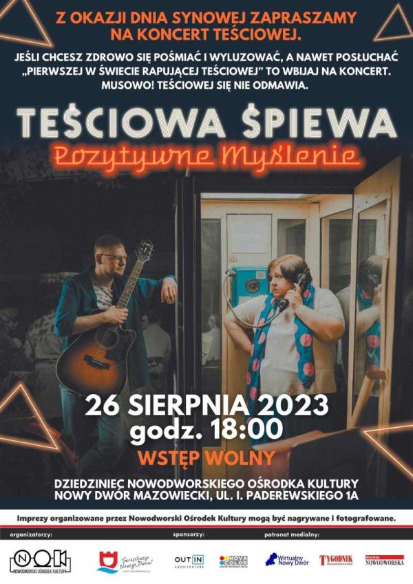 Mężczyzna w okularach z gitarą w prawym ręku oparty lewym przedramieniem o budkę telefoniczną, w której stoi kobieta w jasnej koszulce z niebieskim szalem w różowe koła na szyi rozmawia przez telefon.