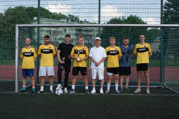 Drużyna piłkarska w żółtych koszulkach z napisem UKS Reduta stojąca w bramce.