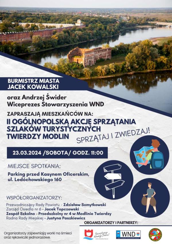 Długi obiekt zabytkowy z czerwonej cegły z biała wieżą. W oddali most kratownicowy. Na pierwszym planie ruiny zabytkowego obiektu z czerwonej cegły pomiędzy dwoma rzekami.