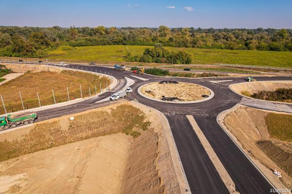 Nowe rondo z pięcioma dojazdami. Na dwóch dojazdach maszyny budowlane i ciężarówki. Na drodze przylegającej samochody osobowe.