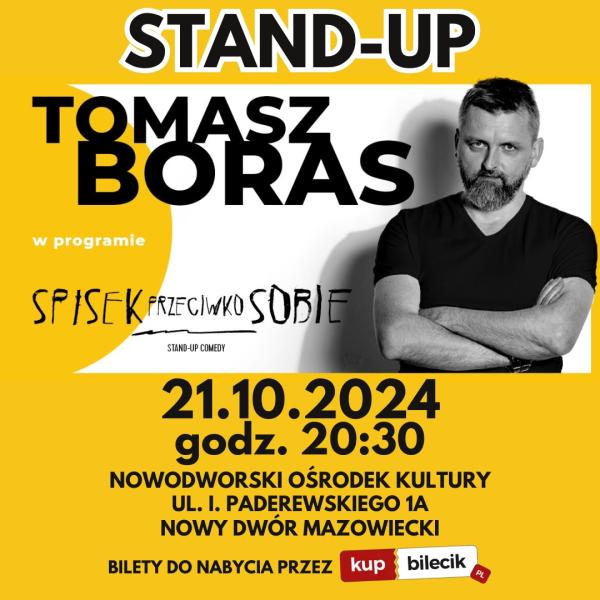 Mężczyzna w czarnych włosach z szpakowatymi wąsami i brodą, ubrany w czarną koszulkę ma założone ręce na brzuchu.