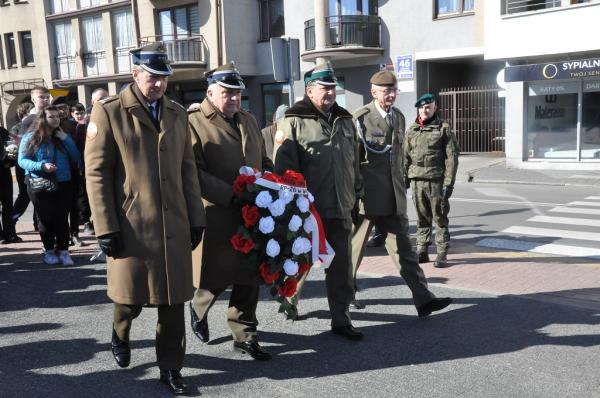 Czterech mężczyzn w mundurach wojskowych. Jeden z nich trzyma wiązankę kwiatów.