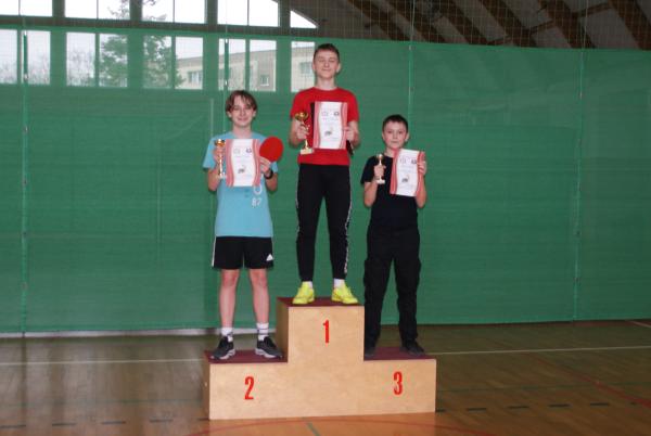 Trzech chłopców stojących na podium i trzymających w dłoniach puchary i dyplomy.