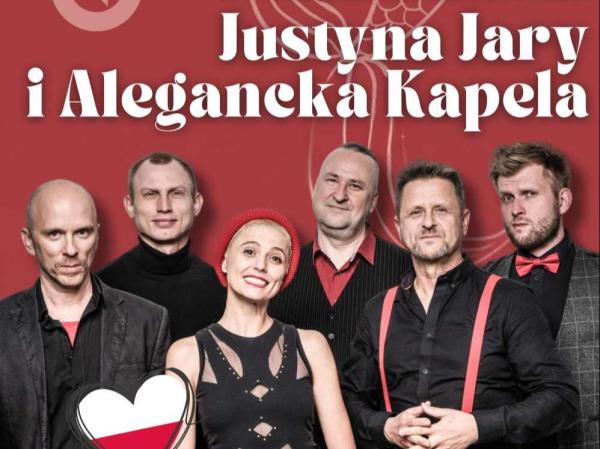 Kobieta i pięciu mężczyzn ubranych na czarno. Po lewej stronie biało-czerwone serduszko.