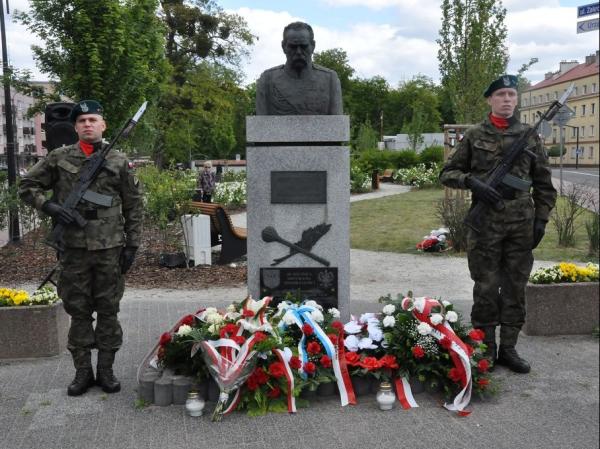 Dwóch mężczyzn w mundurach wojskowych z karabinami na piersiach stoją obok pomnika mężczyzny w mundurze wojskowym.