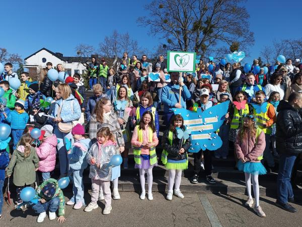 Grupa kilkudziesięciu dzieci z dorosłymi, trzymający balony motyla i transparet z logotypem.